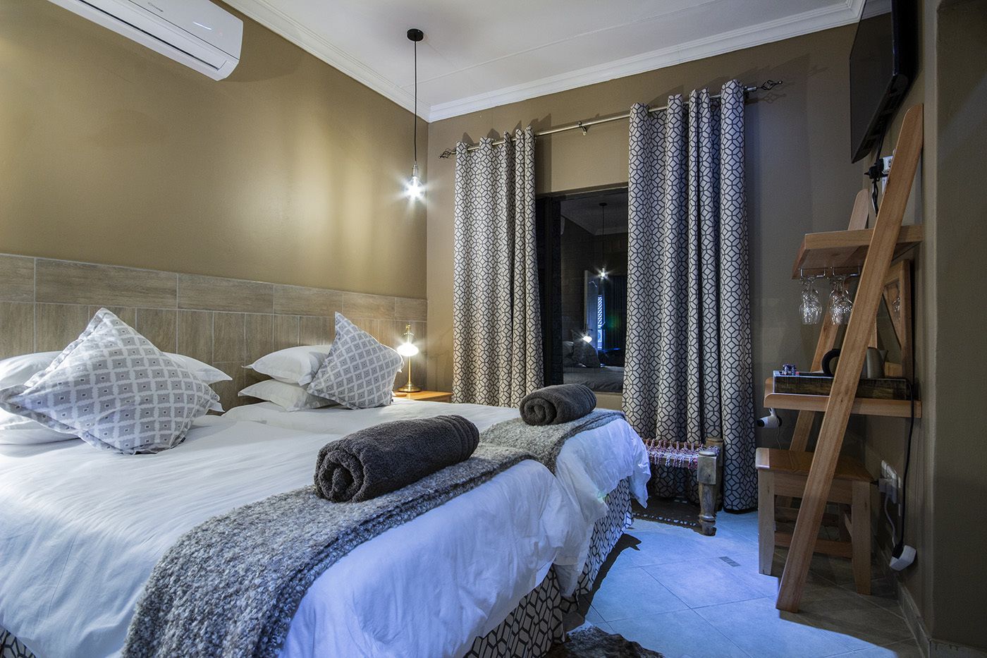 A hotel room with two beds, a TV, a wooden ladder, and a nightstand with a lamp.
