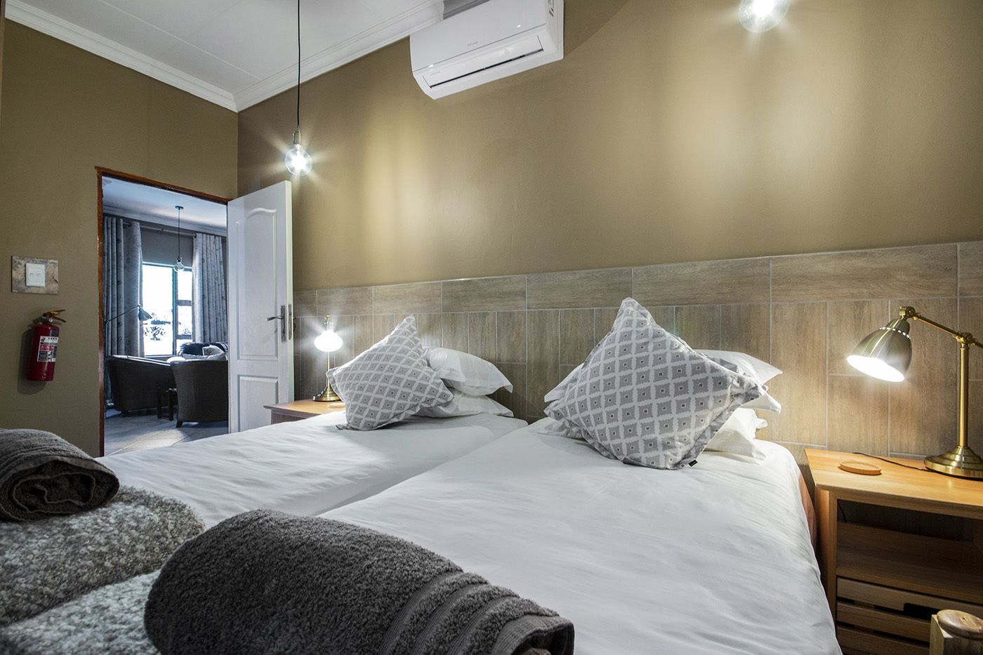 Habitación de hotel con una cama grande, dos lámparas de noche y un cabecero. Hay un extintor en la pared y una ventana con cortinas.