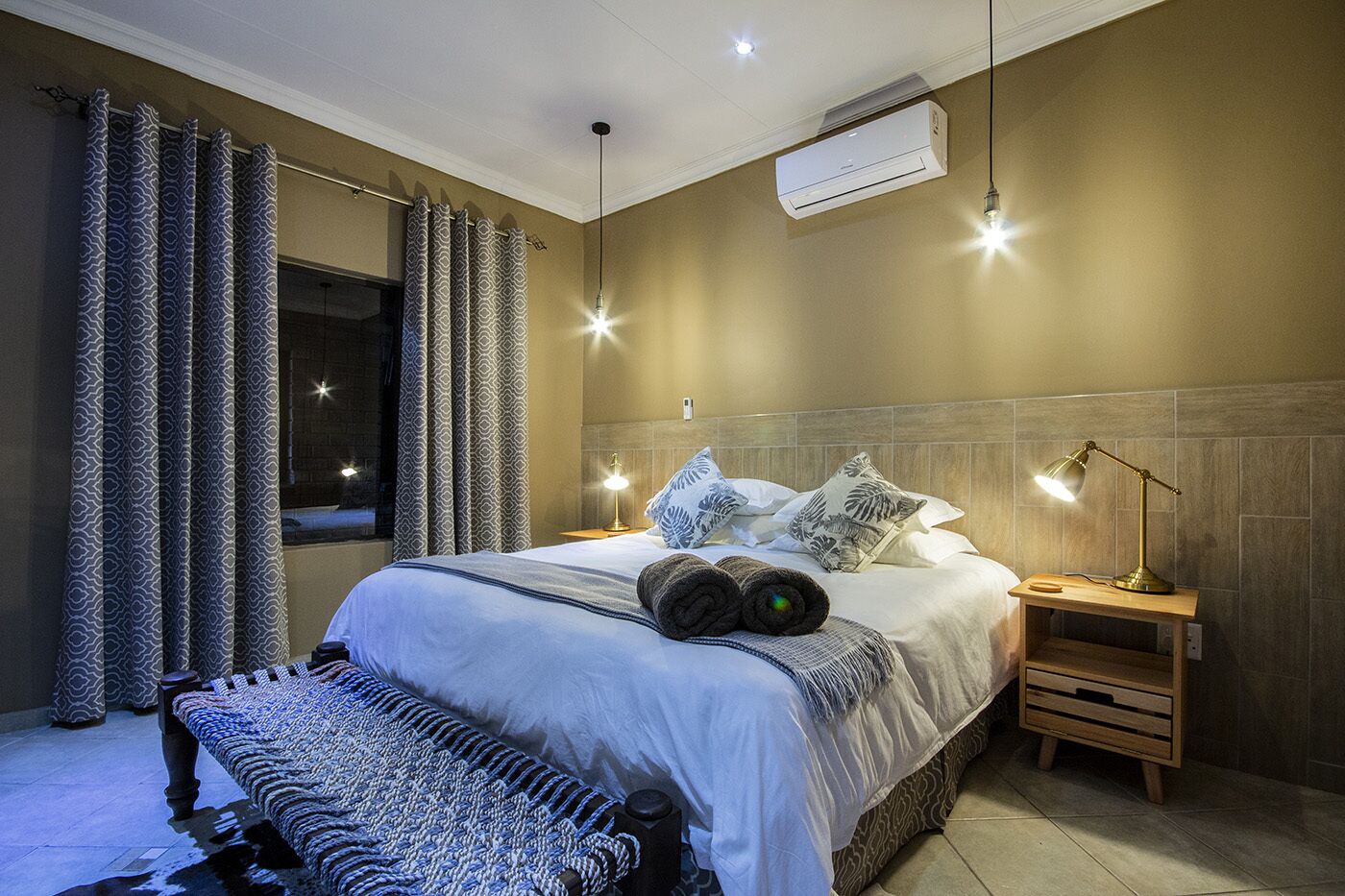 Une chambre à coucher moderne avec un grand lit, des rideaux à motifs, une lampe de chevet et un appareil de climatisation.