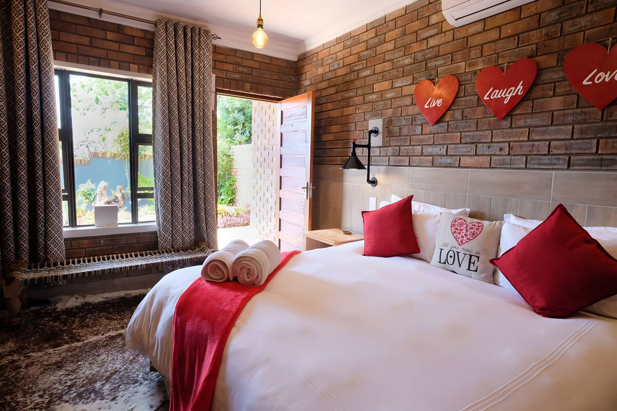 Quarto de hotel com uma cama grande, almofadas vermelhas e decorações em formato de coração na parede.