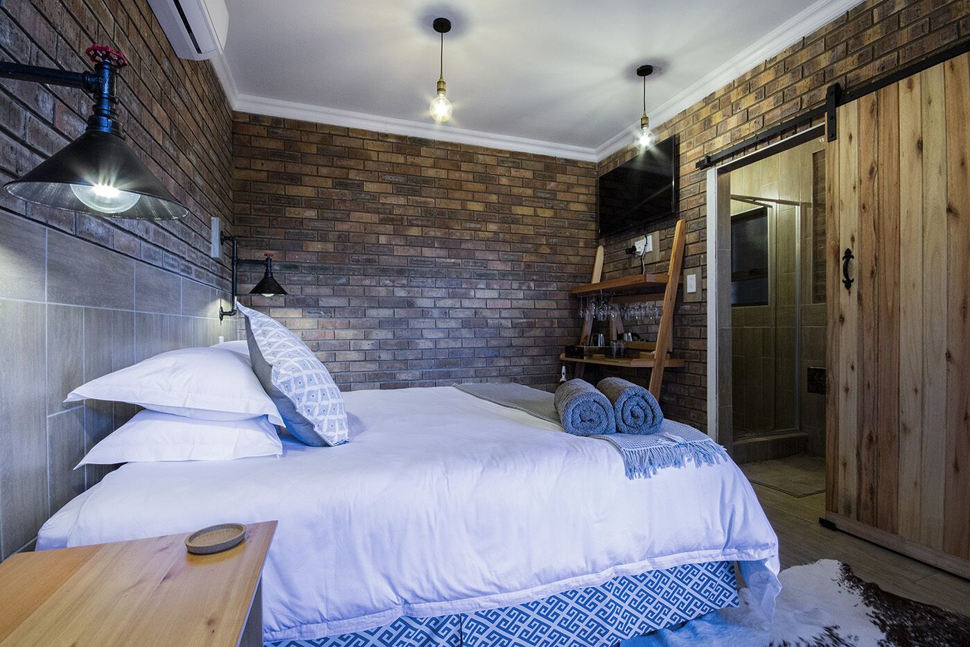 Ein Schlafzimmer mit einer Ziegelwand, einem Bett mit weißer Bettwäsche, einer hölzernen Bank und einer Wendeltreppe zu einem Erkerraum.