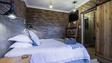 A bedroom with a brick wall, a bed with white bedding, a wooden bench, and a ladder leading to a loft area.