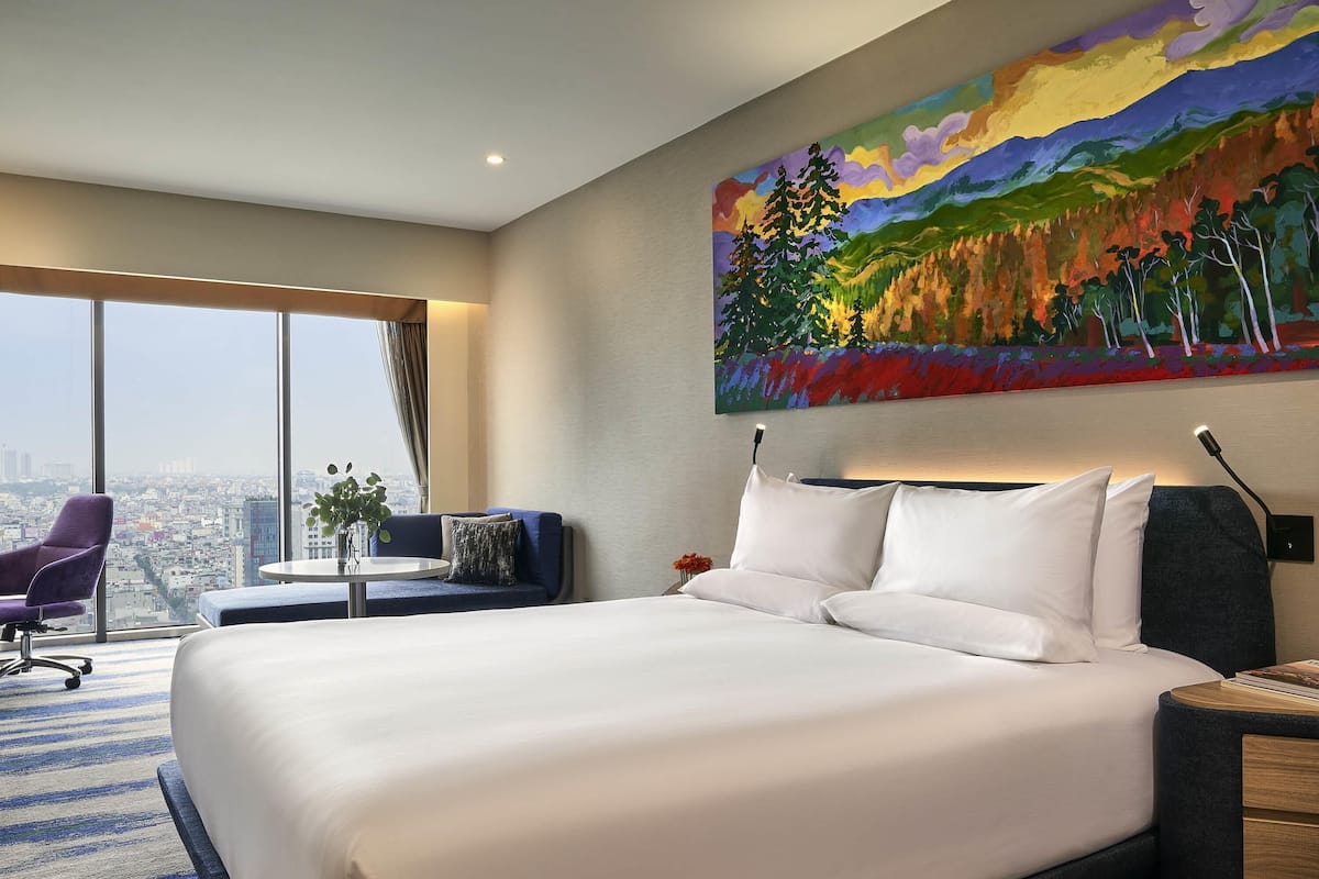 A hotel room with a large bed, a desk, a chair, and a painting on the wall.