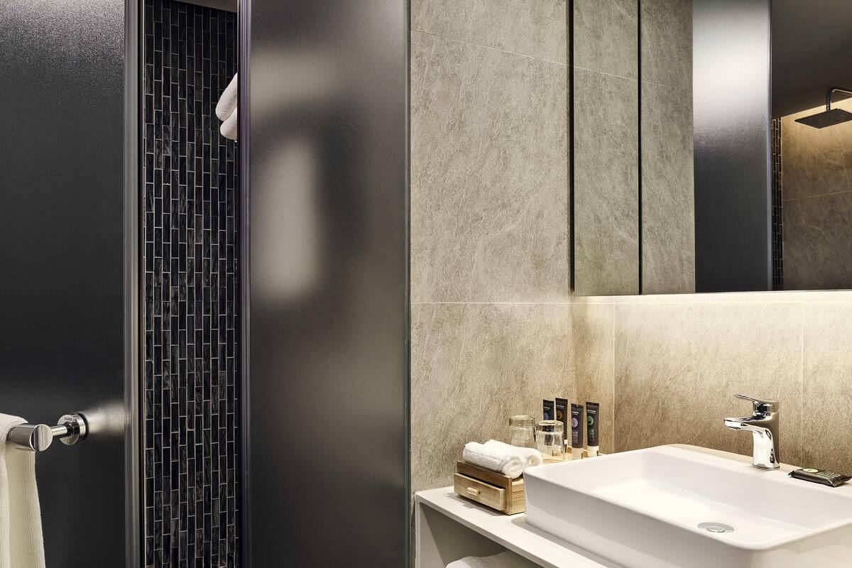 A modern bathroom with a large mirror, a white sink, and a black tiled shower area.