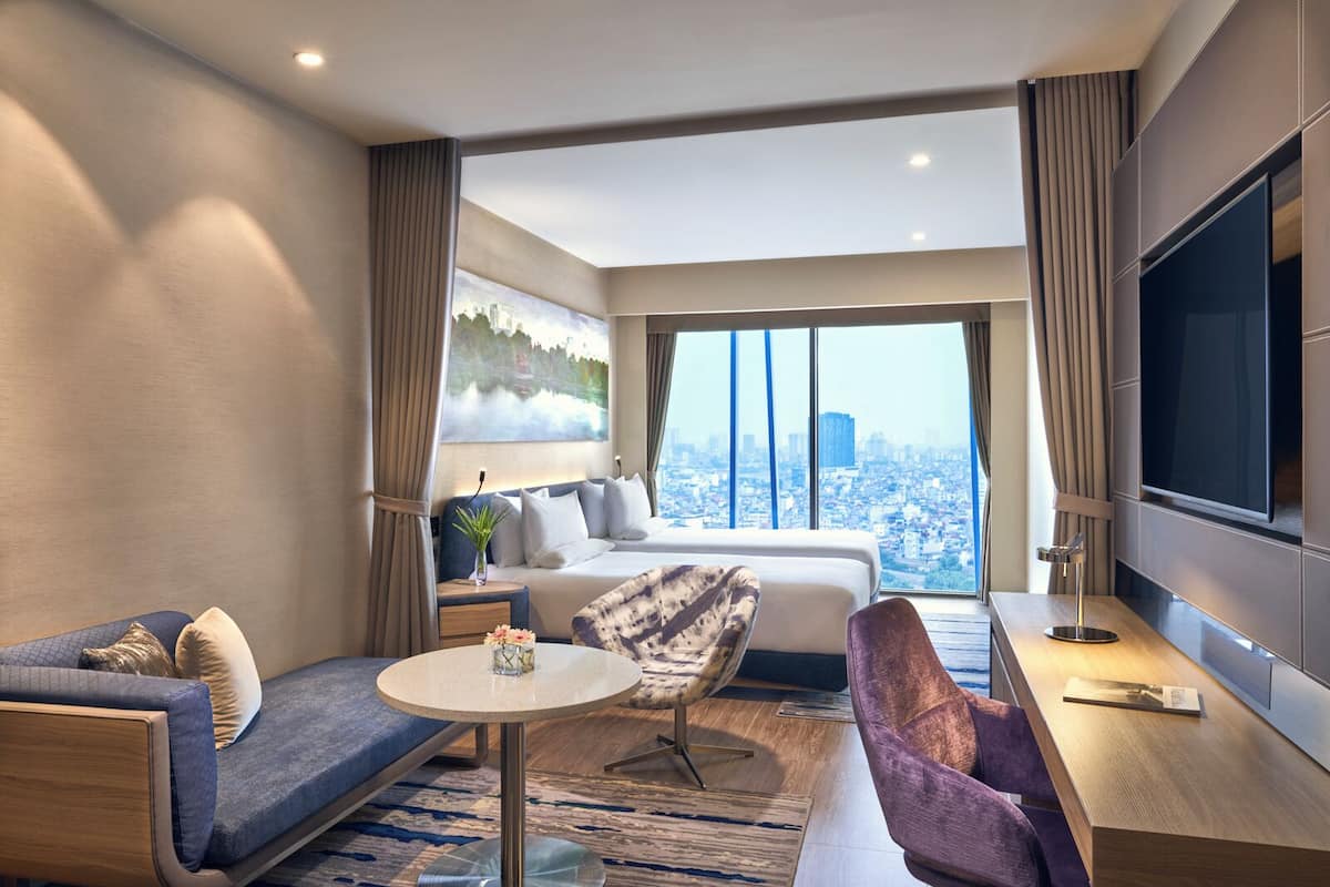 A modern hotel room with a city view, a sofa, a small table, and a TV.