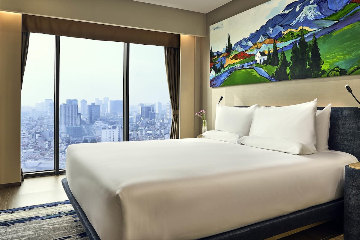 A hotel room with a large bed, a city view, and a colorful painting on the wall.