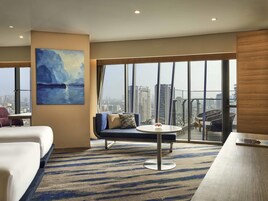 Una habitación de hotel moderna con un ventanal grande, un sofá, una mesa redonda y un cuadro.