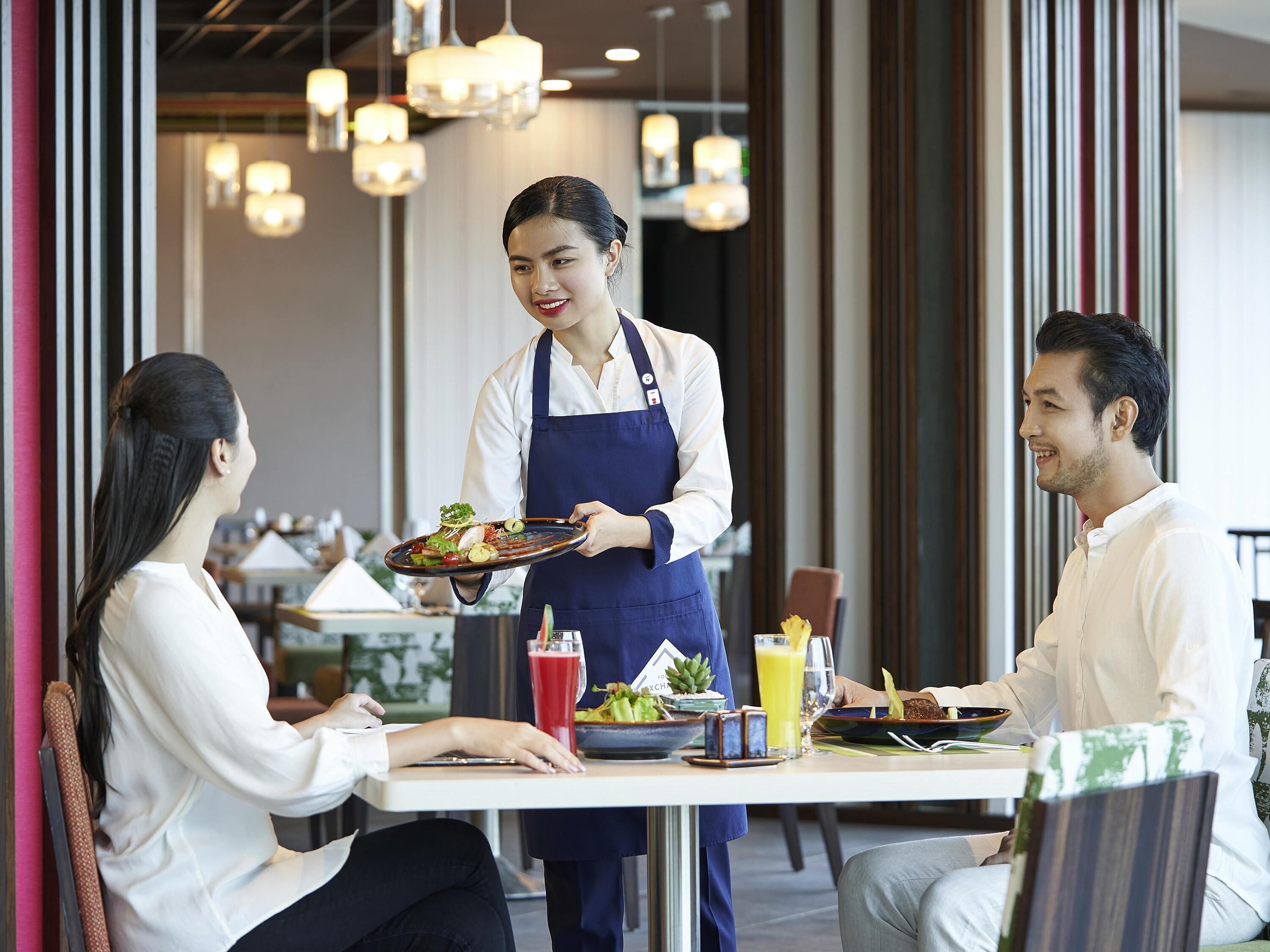 A restaurant setting with a waiter serving food to two diners.