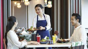 A restaurant setting with a waiter serving food to two diners.