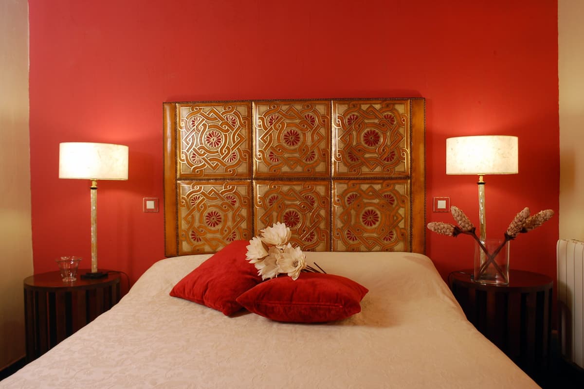 A hotel room with a large bed, red pillows, and two bedside tables with lamps.