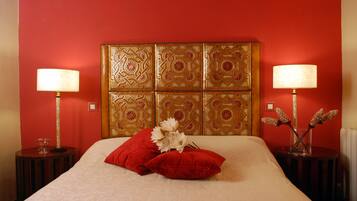 Una habitación de hotel con una cama grande, almohadones rojos y dos mesitas de noche con lámparas.
