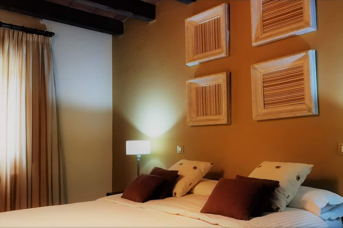 A hotel room with a bed, two bedside lamps, a window with curtains, and four wall-mounted picture frames.