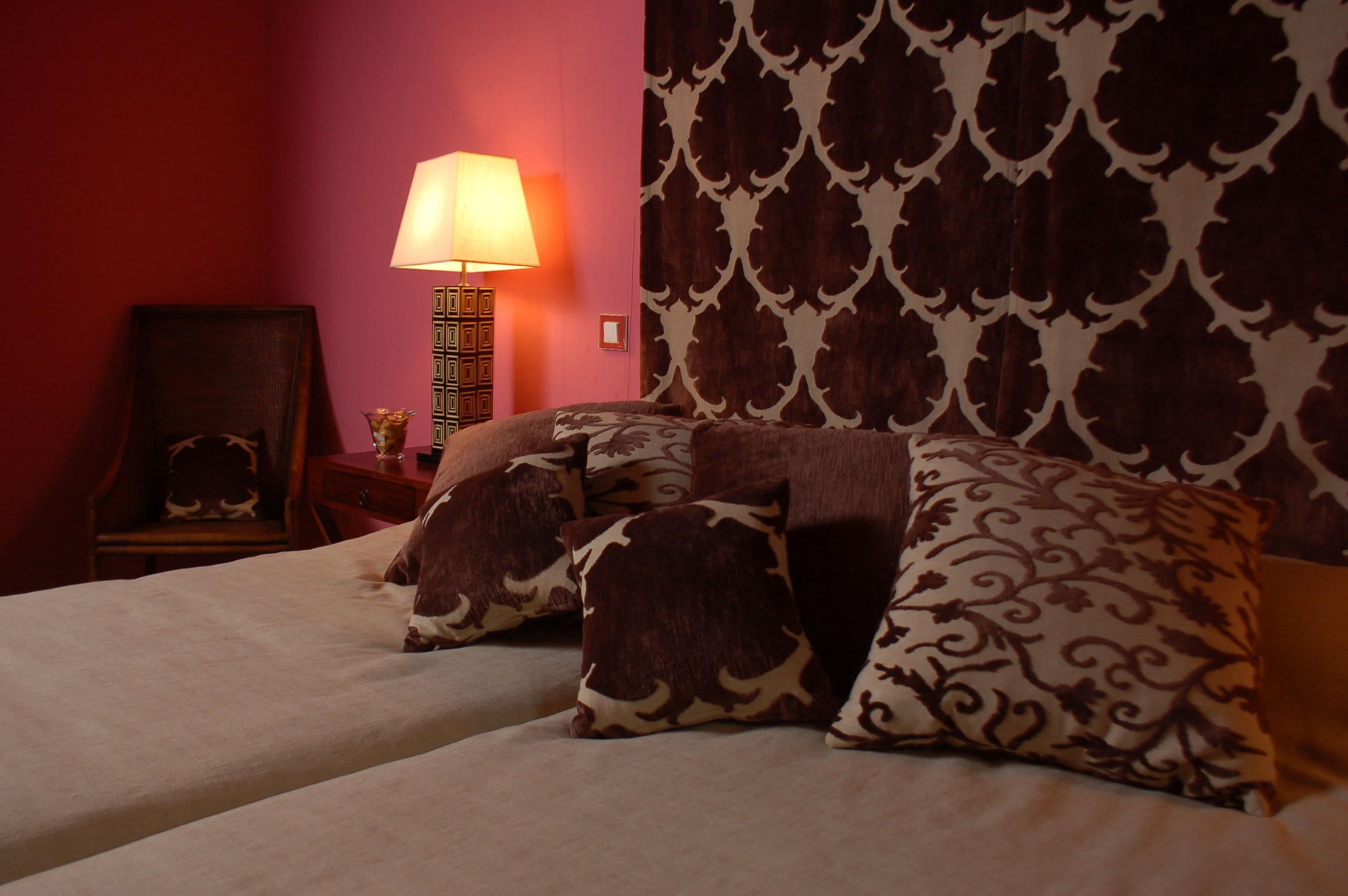 Una cama con almohadas estampadas, una lámpara de noche y un cuadro en la mesita.