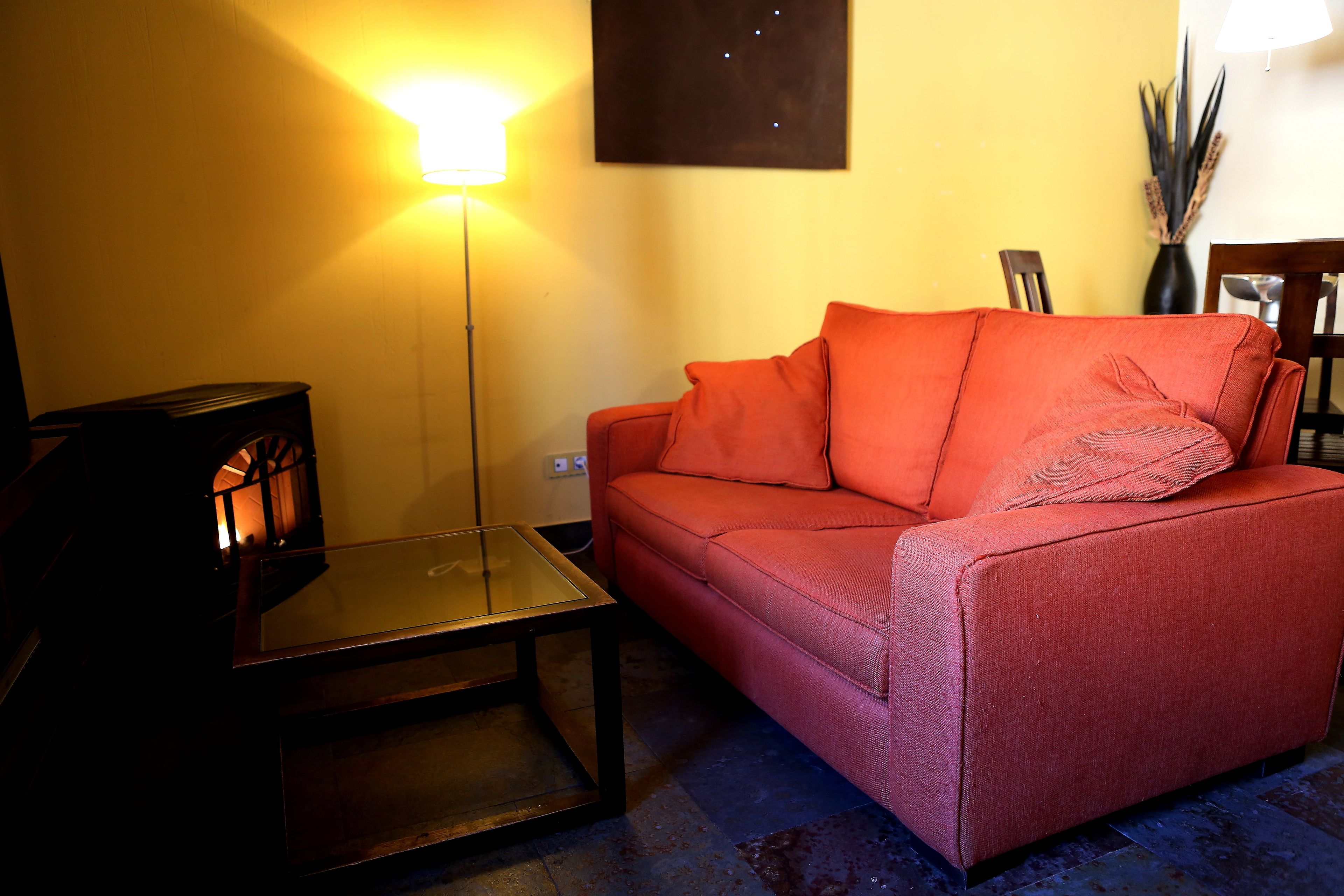 Una sala de estar con un sofá rojo, una mesa de centro de vidrio, una lámpara de pie y un mueble bajo de madera oscura.