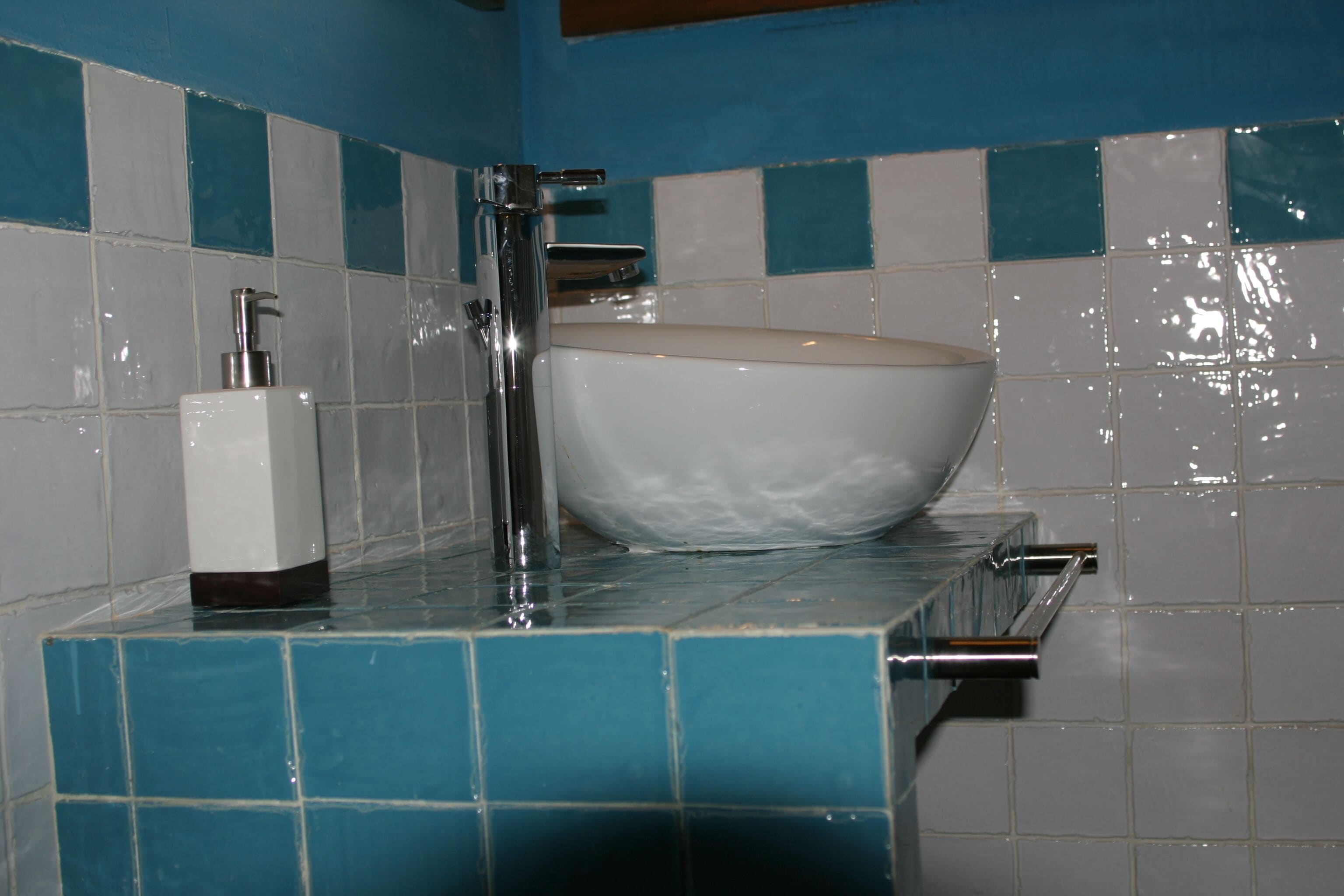 Un baño con lavamanos blanco, grifo de cromo y dispensador de jabón en la encimera.