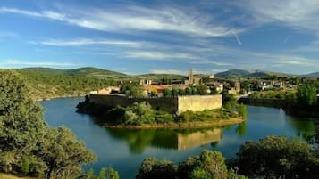 Una fortificació històrica envoltada per un riu tranquil, vegetació exuberant i turons allunyats.