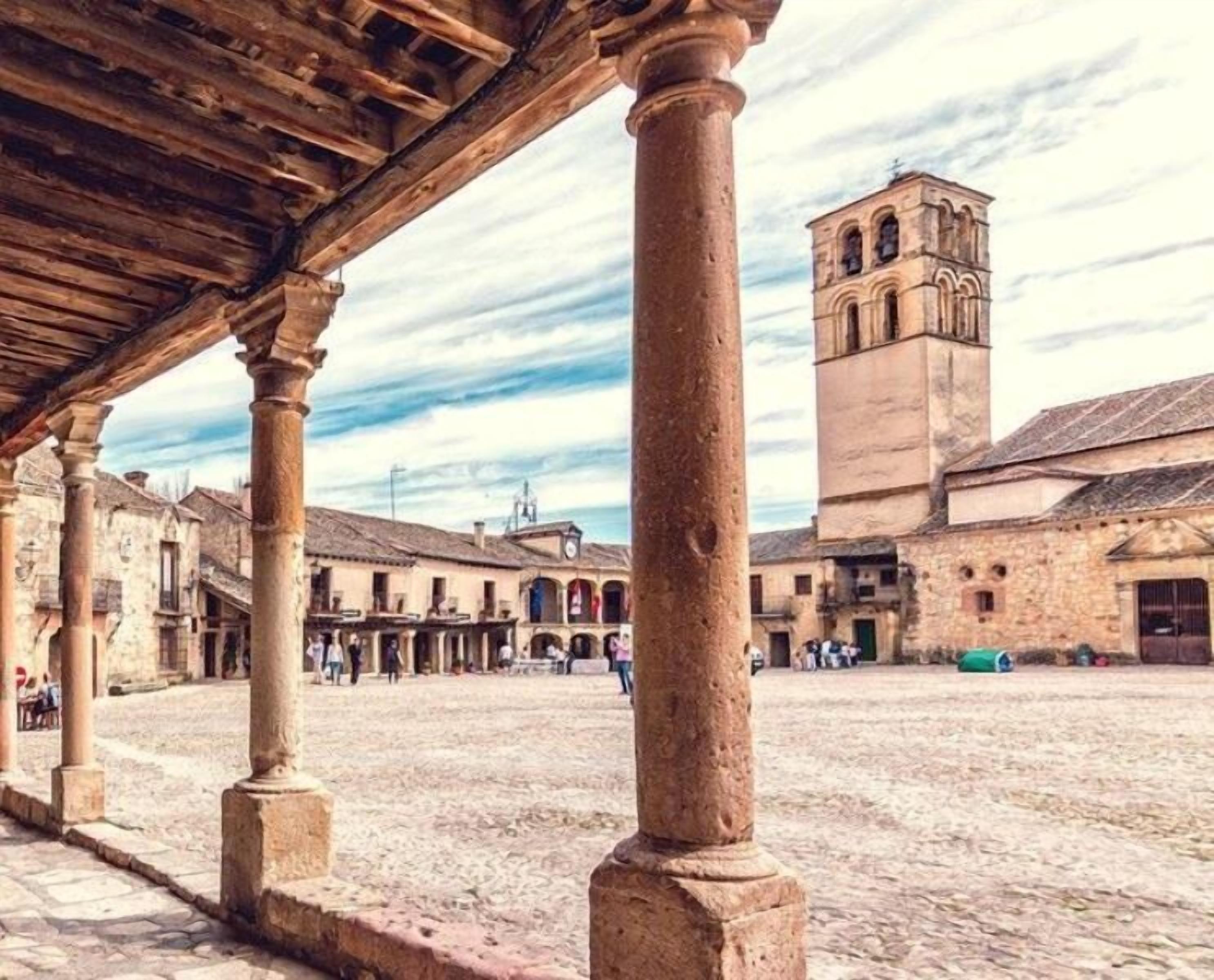 Une cour bordée de colonnes en pierre, une allée couverte et un bâtiment historique avec un clocher en arrière-plan.