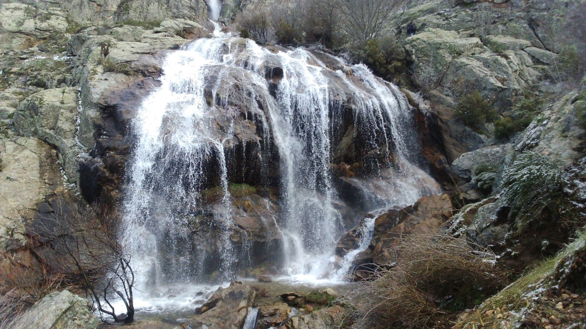 A waterfall cascading over rocky terrain with sparse vegetation.