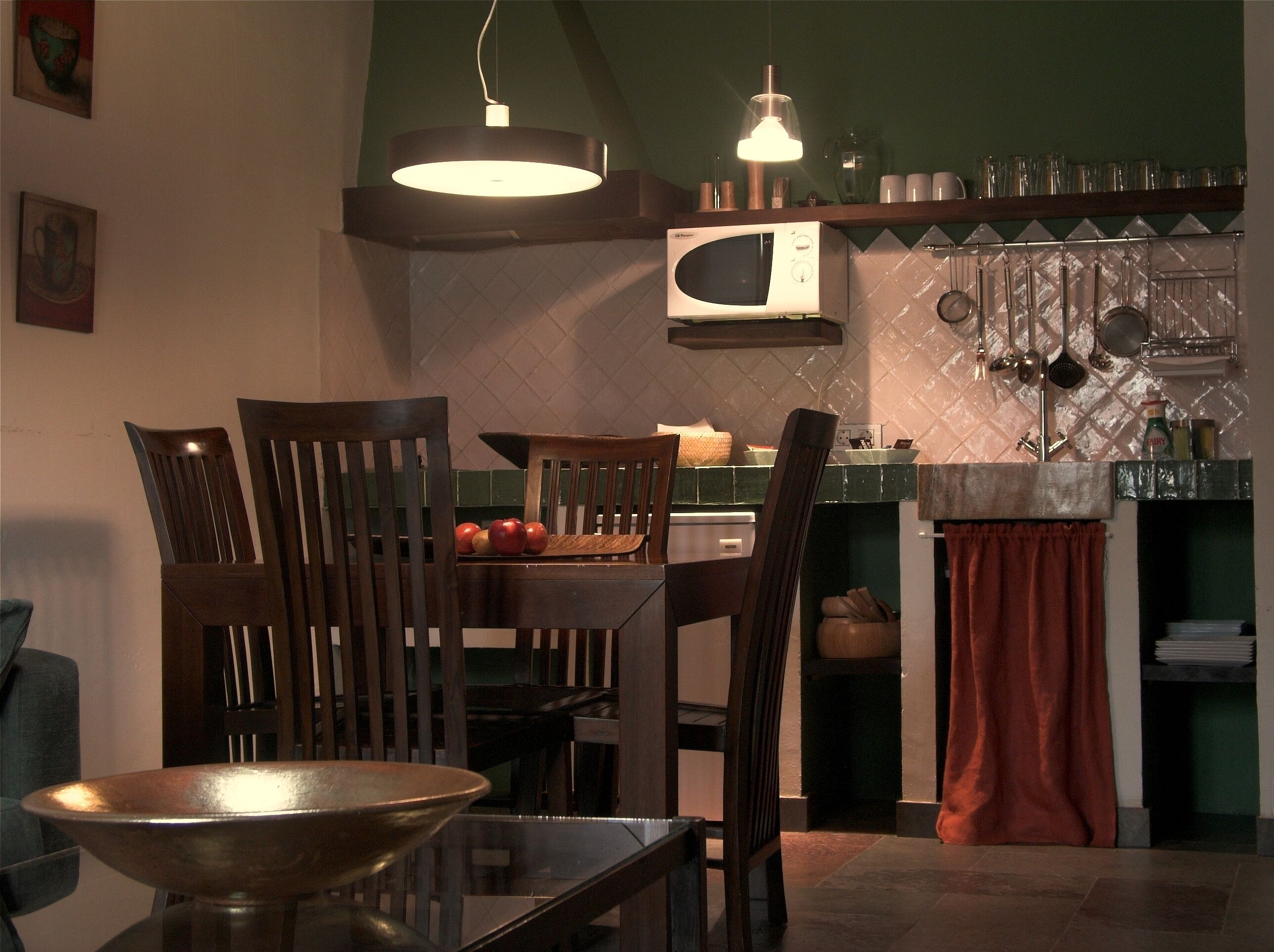 Un comedor con sillas de madera, una mesa, un bol, un microondas y utensilios de cocina colgando.