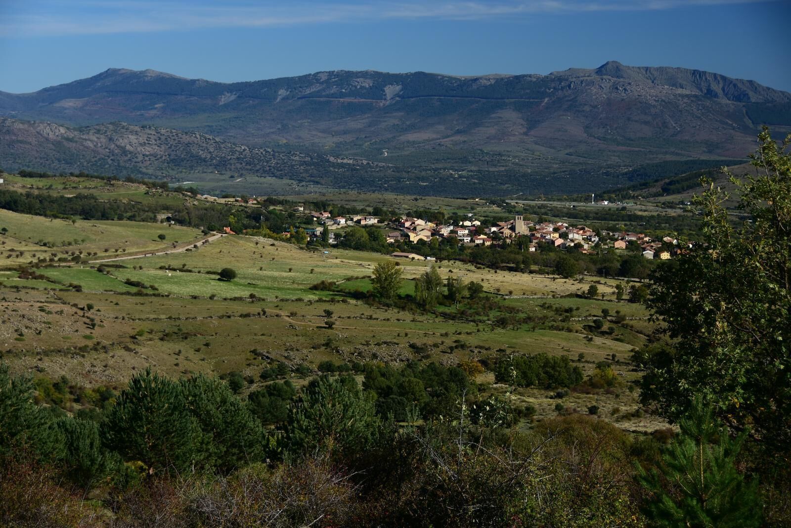 Un paisaje rural con un pueblo enclavado entre colinas y montañas ondulantes.