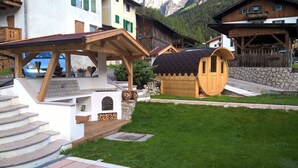 A chalet-style building with a wooden deck, stone steps, and a small wooden structure with a sloped roof. - Residence Le Rose (San Giovanni di Fassa)