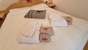 A neatly made bed with a wooden headboard, a decorative pillow, and several neatly folded towels with a rose design. - Residence Le Rose (San Giovanni di Fassa)