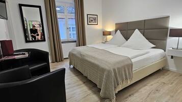 Une chambre d’hôtel comprenant un lit, des lampes de chevet, un bureau avec une chaise, un miroir et une fenêtre avec des rideaux.