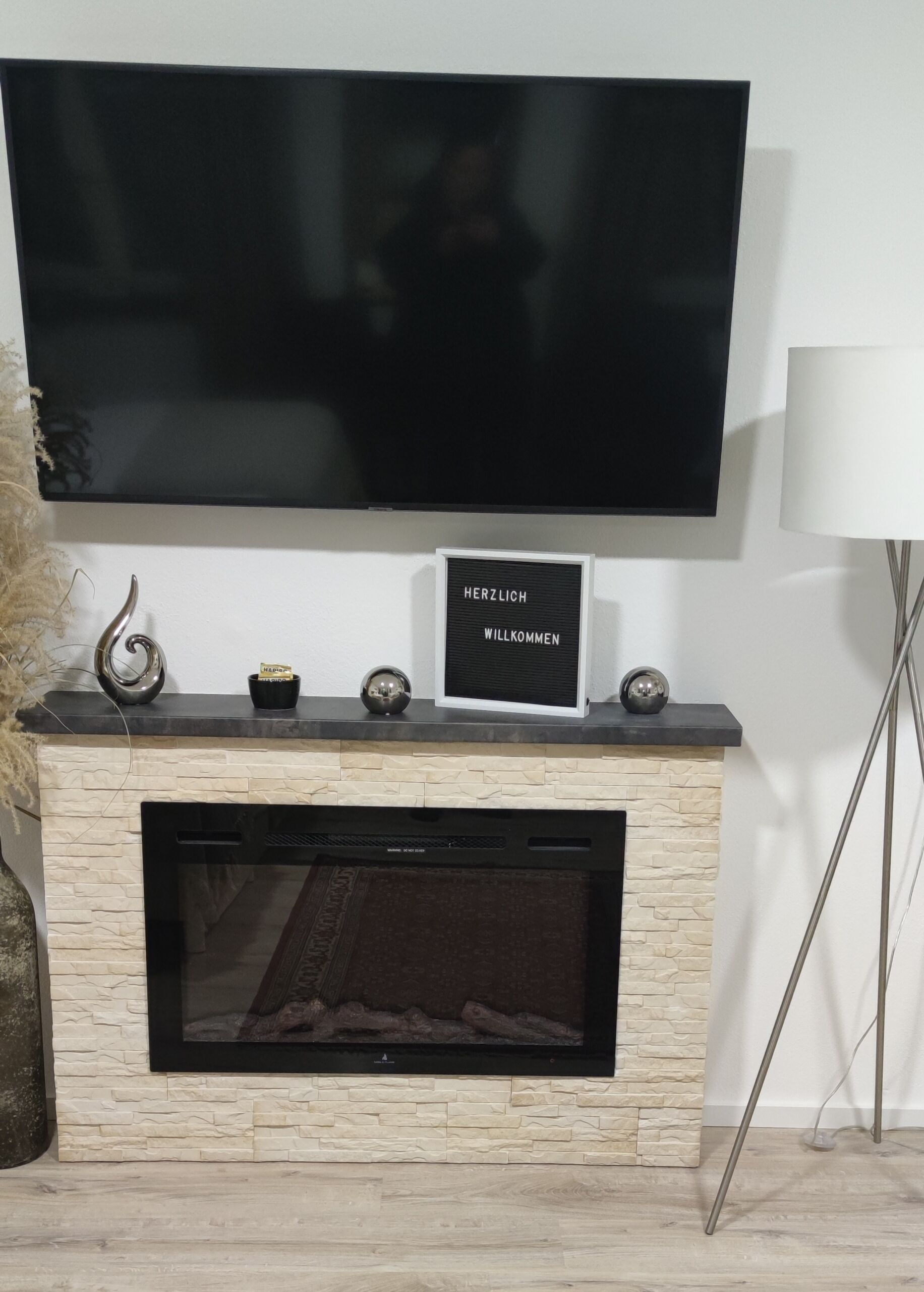 Una sala de estar moderna con un televisor de pantalla plana sobre la chimenea, un letrero decorativo y una lámpara de pie.
