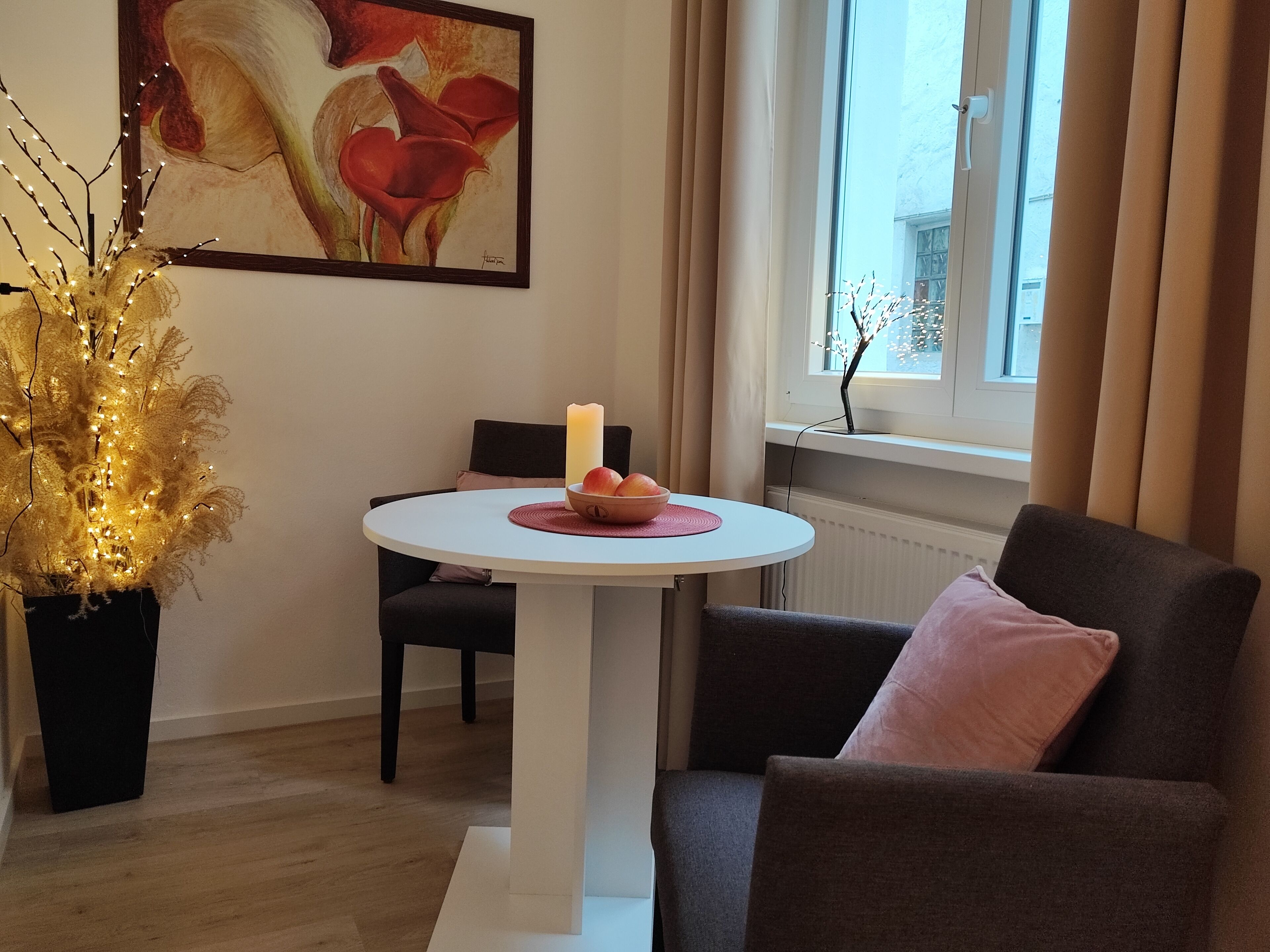 Ett modernt vardagsrum med ett runt, vitt bord, en mörk fåtölj, en beige soffa, en prydnadsväxt och en tavla på väggen.