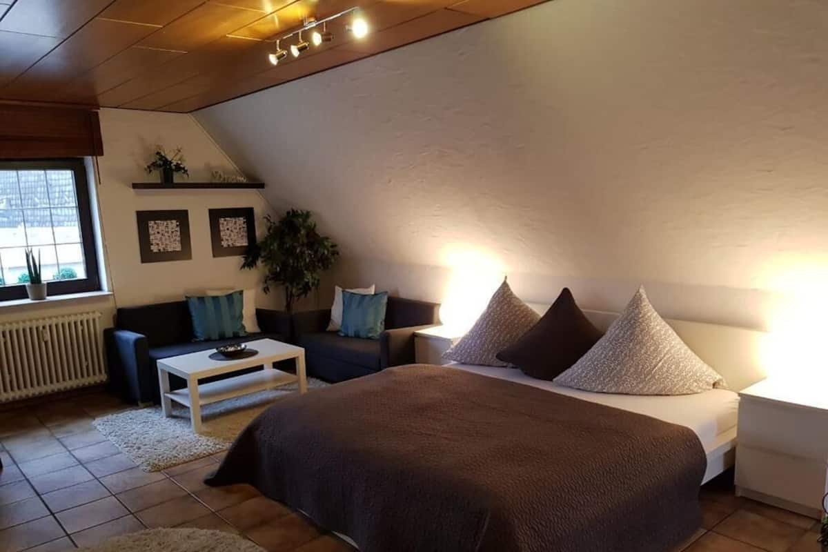 A bedroom with a large bed, a sofa, a coffee table, and a window with a view.