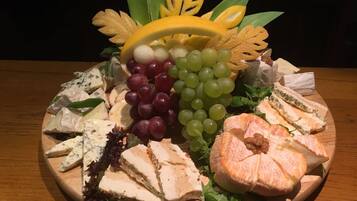 A wooden platter with various cheeses, grapes, and leafy greens.