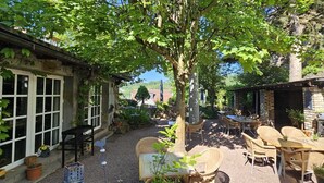 A rustic outdoor seating area with wicker furniture, a stone building, and a tree providing shade. - Hotelbetriebe Güldenhaupt Gmbh (Arnsberg)