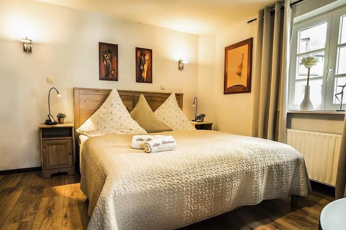 A neatly arranged hotel room with a large bed, a bedside table, a nightstand, and a window with curtains.