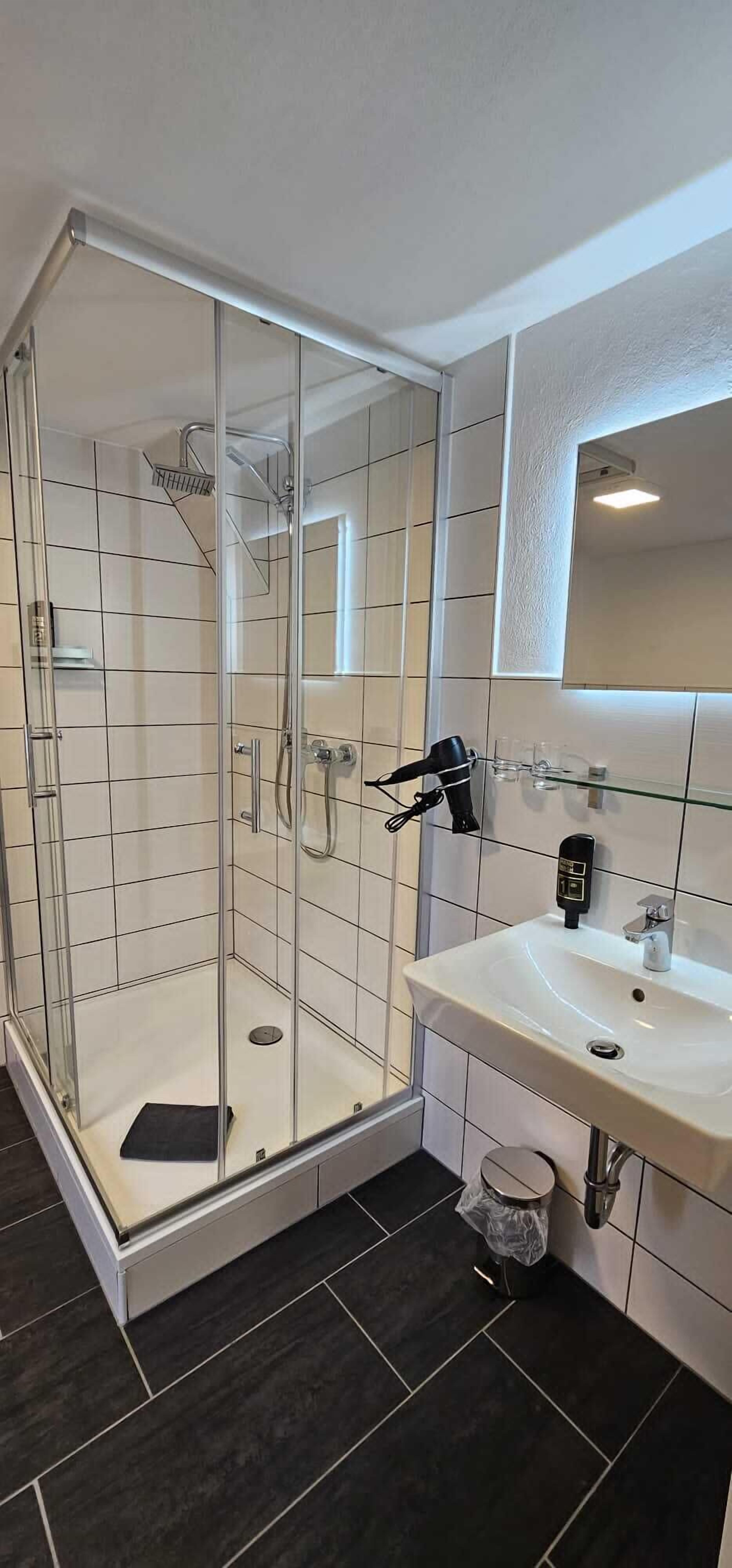 Een moderne badkamer met een douchecabine van glas, een wit wastafelmeubel met spiegel en donkere betegelde vloer.