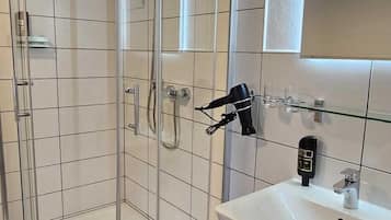 Een moderne badkamer met een douchecabine van glas, een wit wastafelmeubel met spiegel en donkere betegelde vloer.