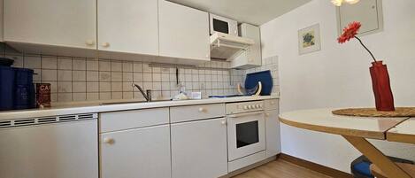A compact kitchen with white cabinets, a built-in microwave, and a small oven.