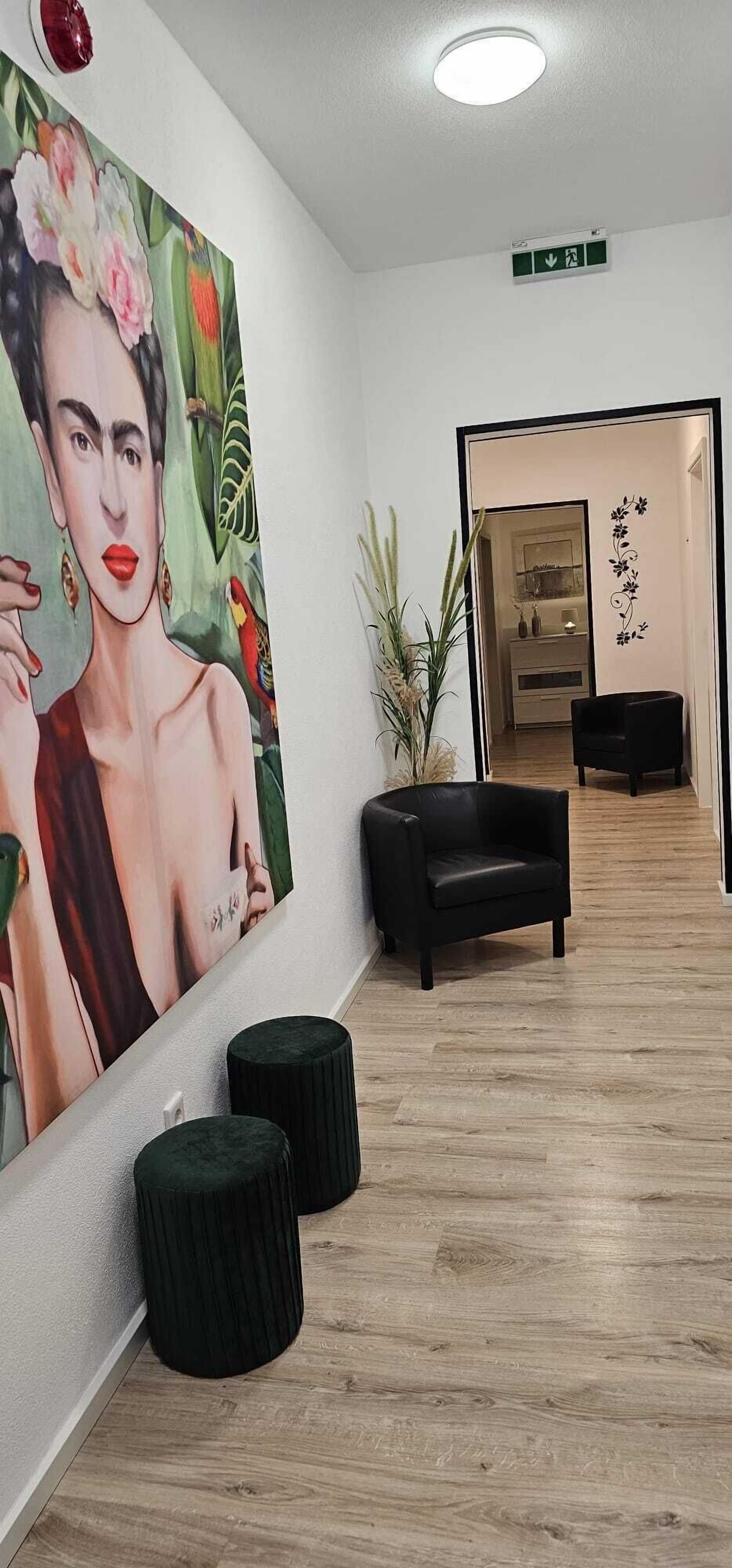 Un pasillo con un cuadro grande, un sofá negro y una planta en maceta.