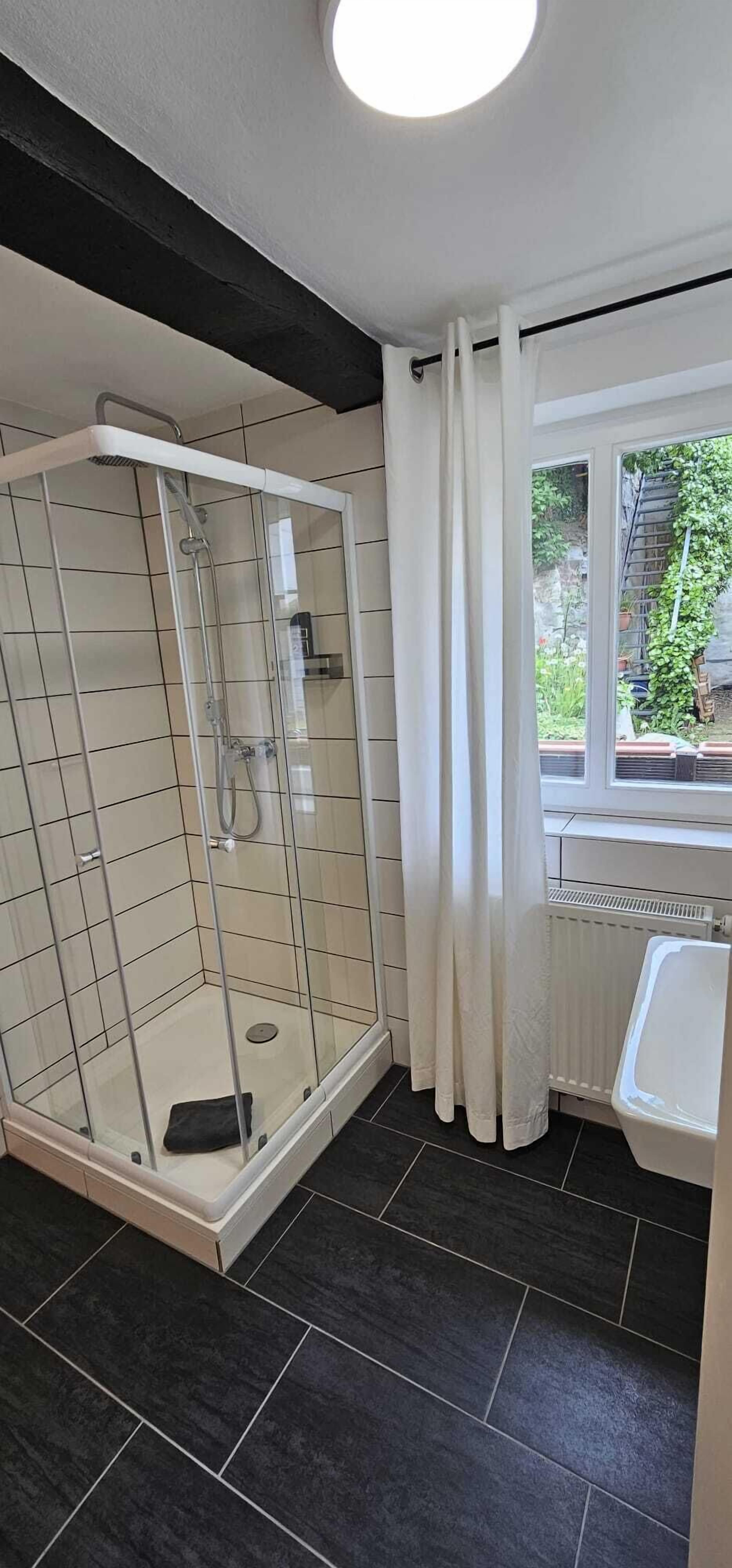 Un baño moderno con ducha envuelta en vidrio, una bañera blanca y una ventana con cortinas.