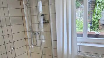 Un baño moderno con ducha envuelta en vidrio, una bañera blanca y una ventana con cortinas.