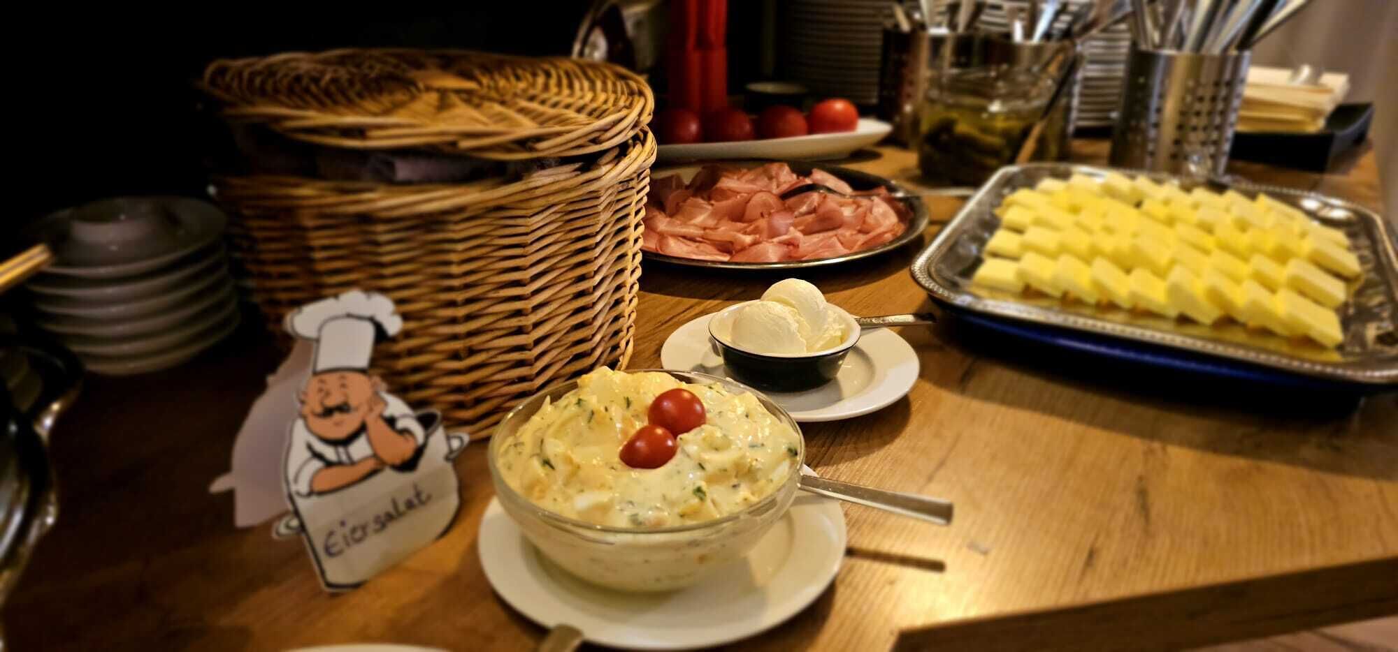 Ett buffébord med olika rätter, inklusive en stor skål med sallad, skivad skinka och ett fat med osttärningar.