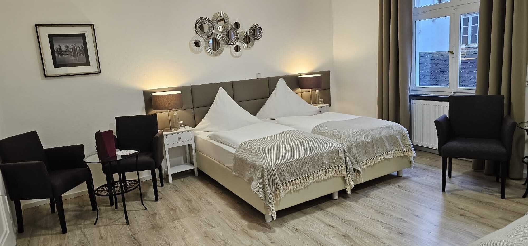 Ein Hotelzimmer mit einem Bett, zwei Nachttischen, einem Sessel, einem kleinen Tisch und einem Fenster mit Vorhängen.