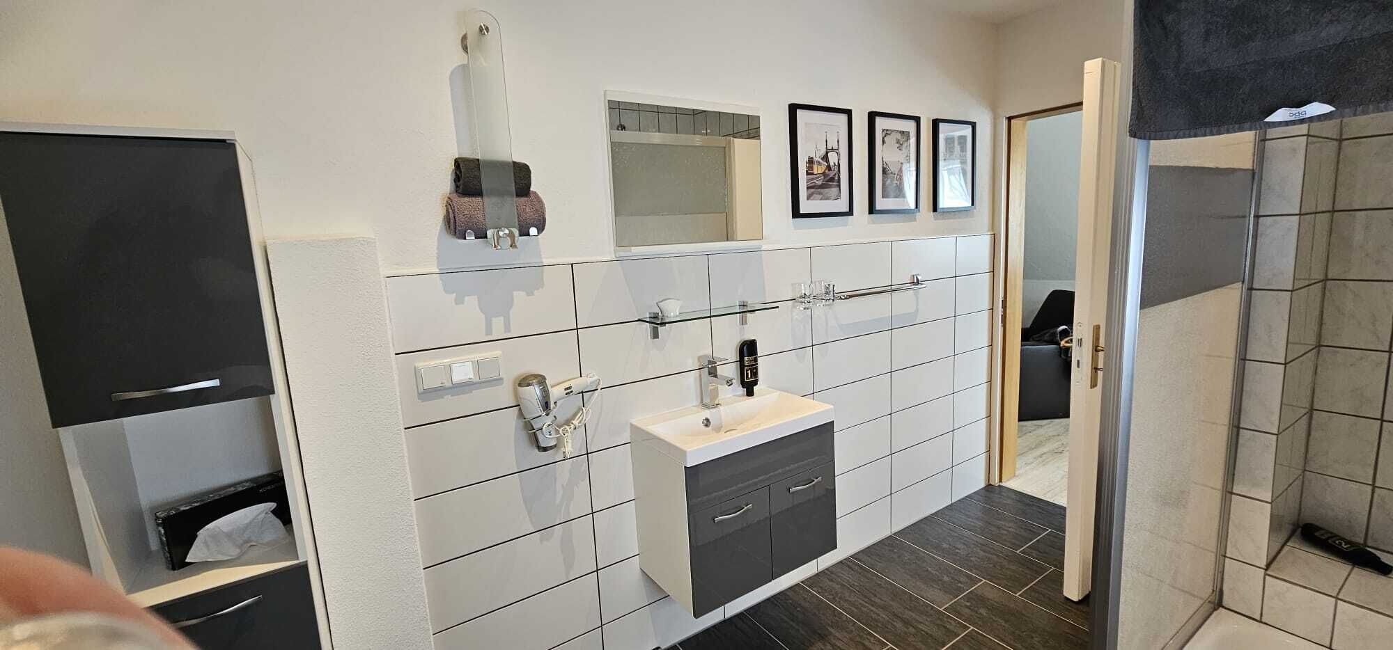 A modern bathroom with a white and gray color scheme, a mirror, a sink, and a shower area.