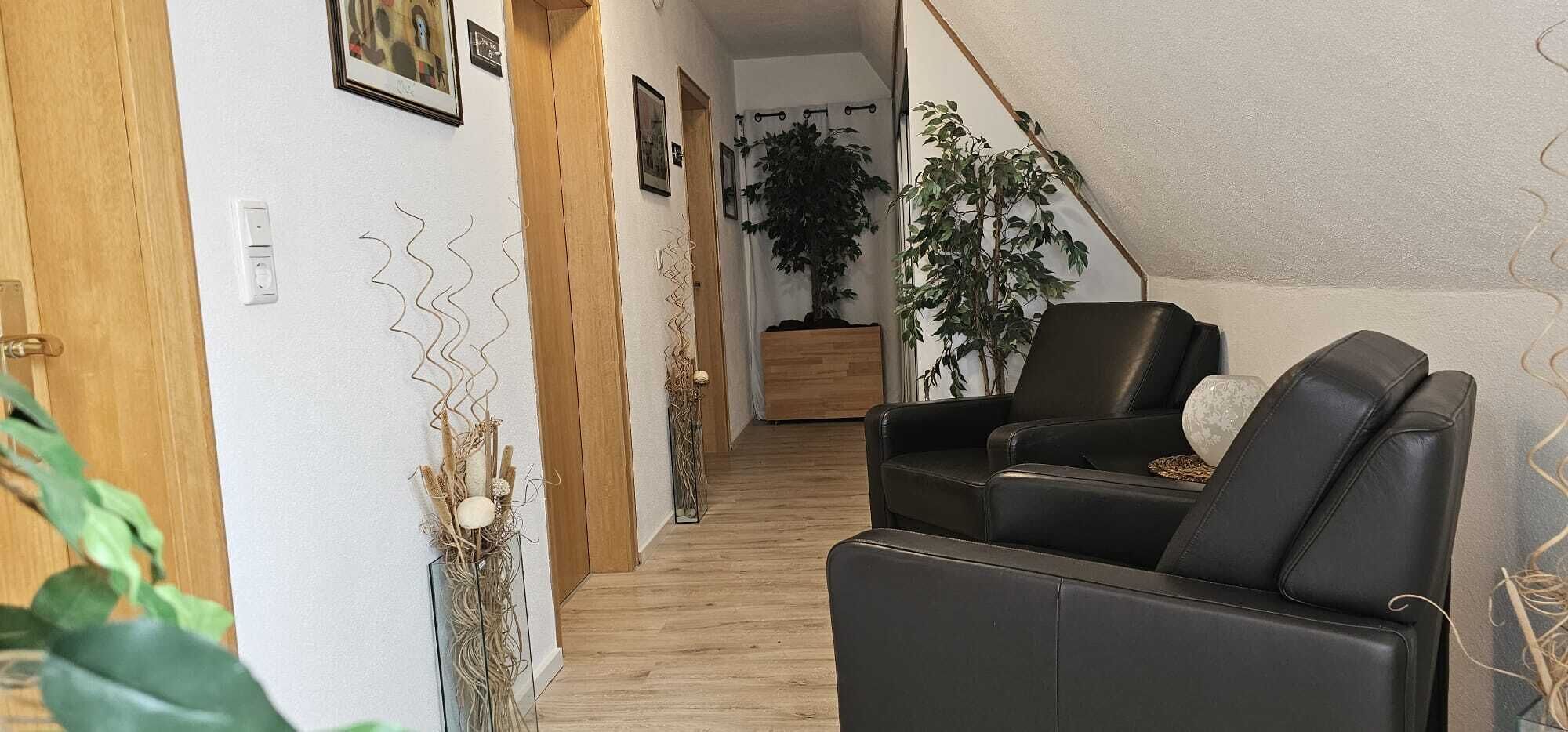 Un couloir avec une porte en bois, un canapé en cuir noir et une plante en pot.