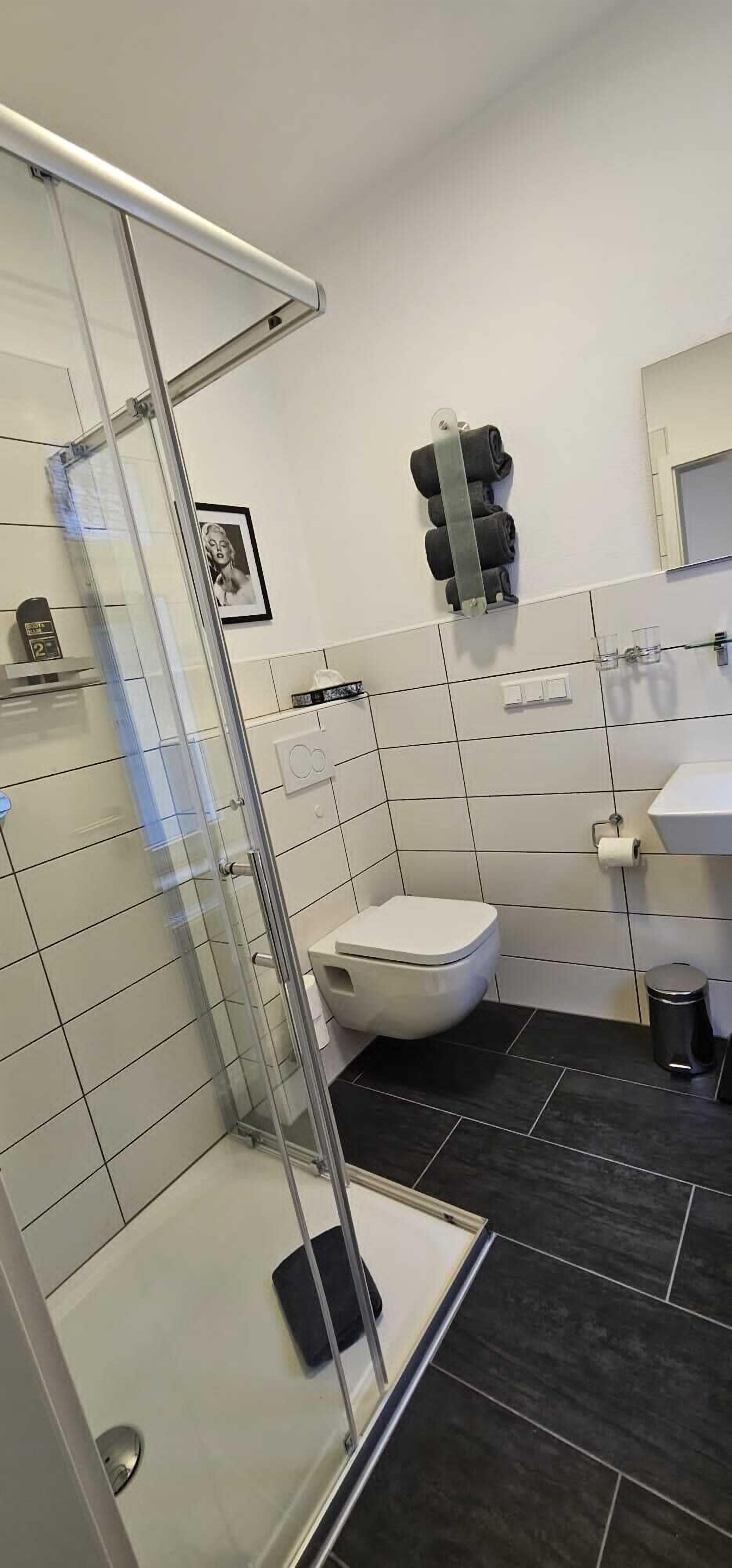 A modern bathroom with a glass shower enclosure, a toilet, a sink, and a towel rack.