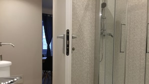 A bathroom with a white bathtub, a glass-enclosed shower, and a door leading to a dining area. - Le Fate Suites (Rome)