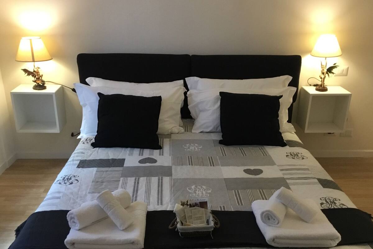 A neatly made bed with a checkered bedspread, two black and white pillows, and two bedside tables with lamps.