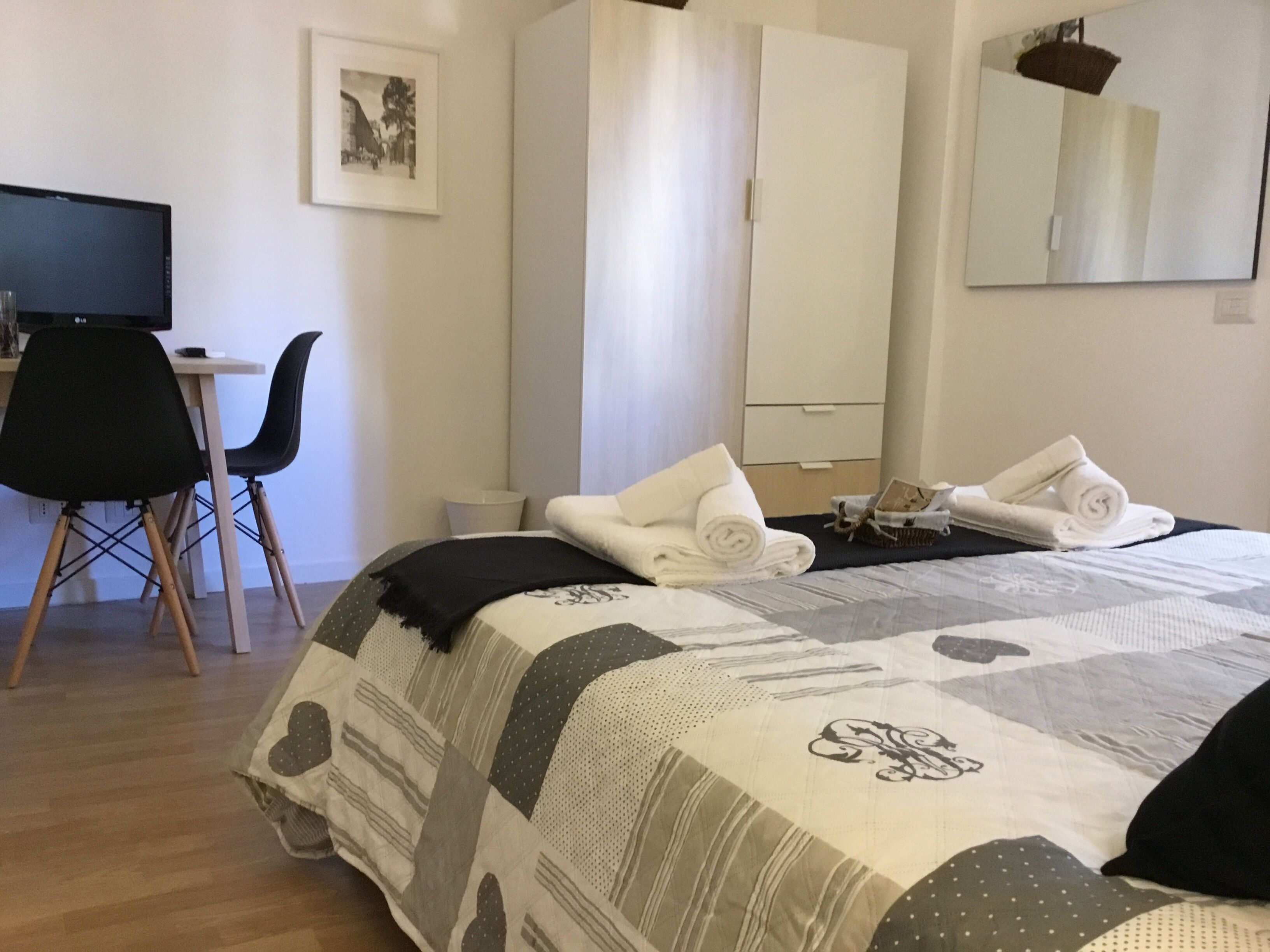 A hotel room with a bed, a desk, a chair, a wardrobe, and a mirror.