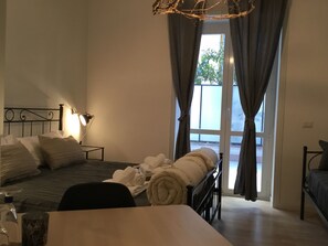 Une chambre à coucher avec un lit, une table de chevet, une lampe et une vue sur l’extérieur, visible à travers une fenêtre avec des rideaux.