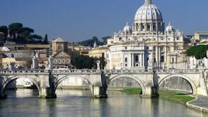 A bridge with multiple arches over a river, leading to a large historical building with a dome. - Le Fate Suites (Rome)