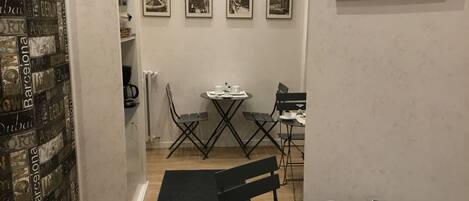 Un comedor con una mesa dispuesta para dos personas, una silla negra y una silla plegable negra. Hay cuatro cuadros enmarcados en la pared sobre la mesa.